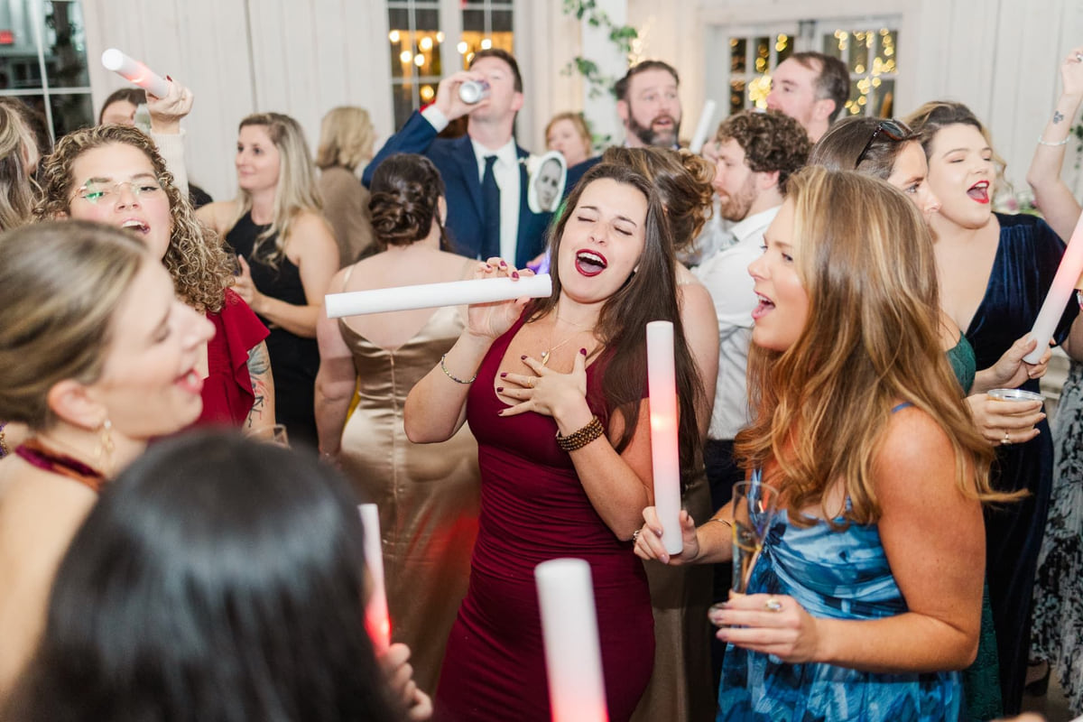 Wedding guests singing and dancing with glowing foam batons at a packed reception