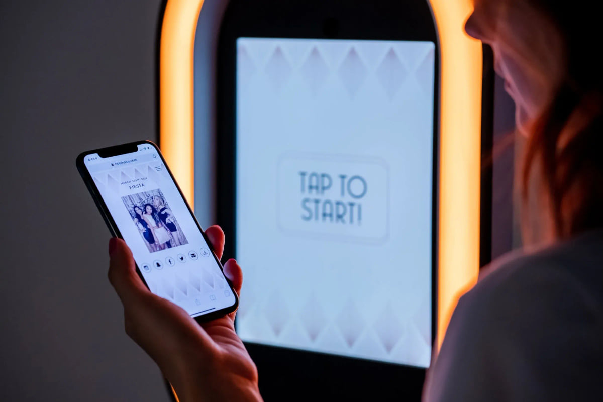 A guest holding a phone showing the photo they just took, the lit booth screen behind them