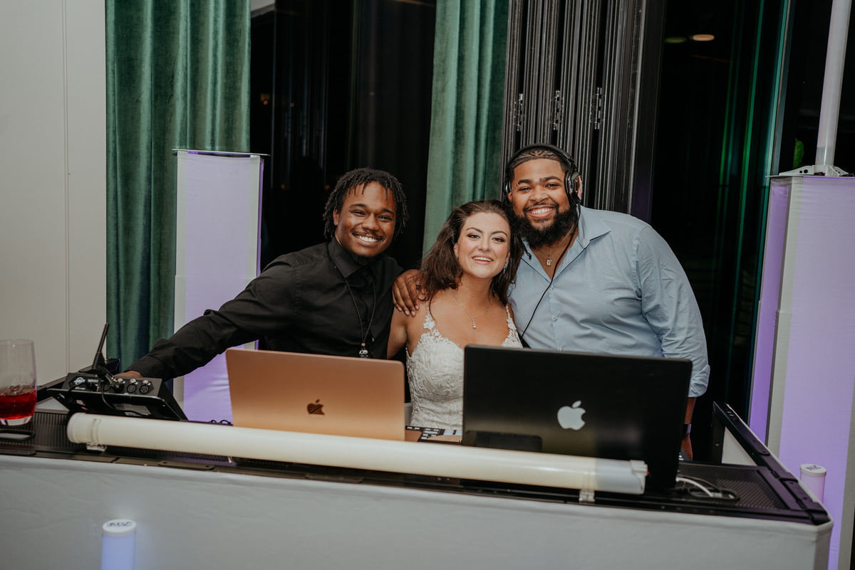 People gathered behind a DJ booth set with two laptops and a speaker