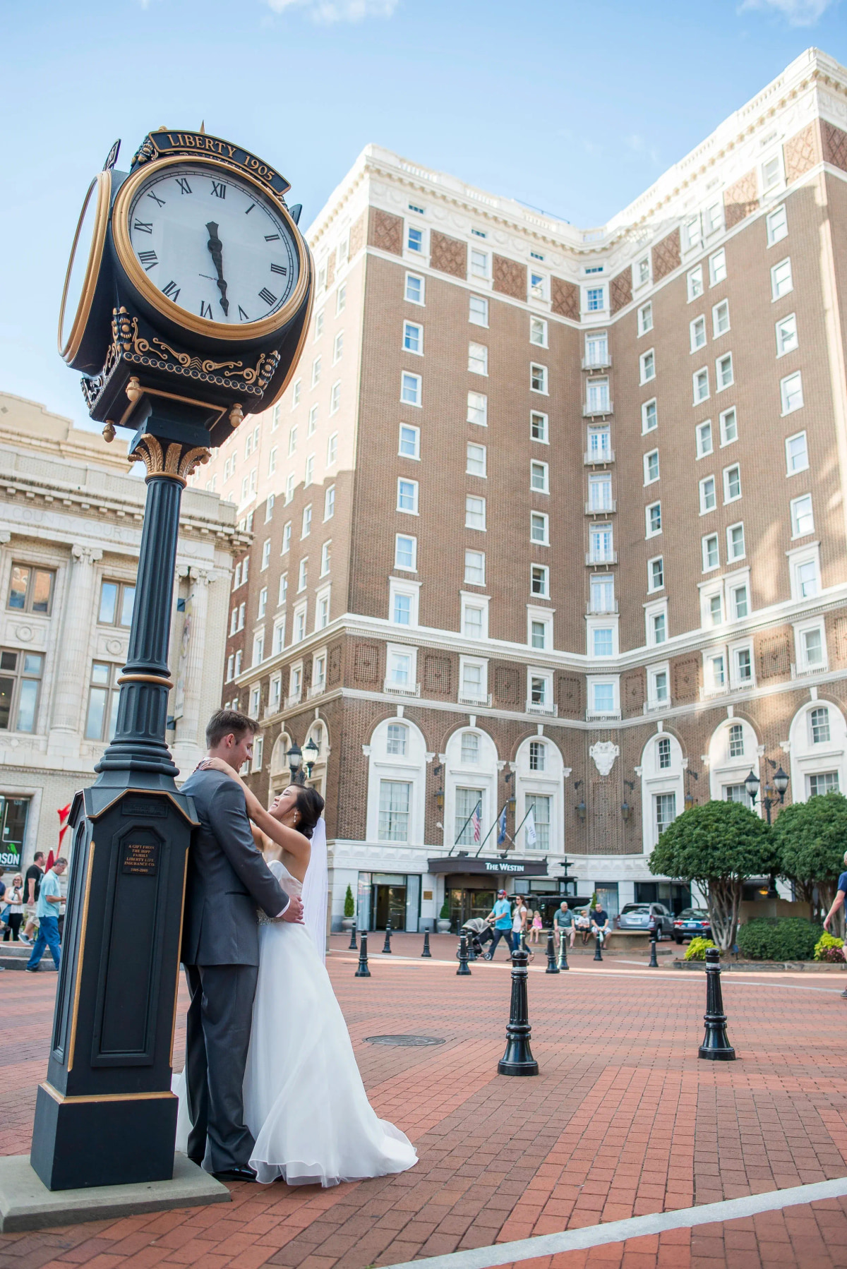 A couple embracing on a downtown sidewalk beside a cast iron street clock