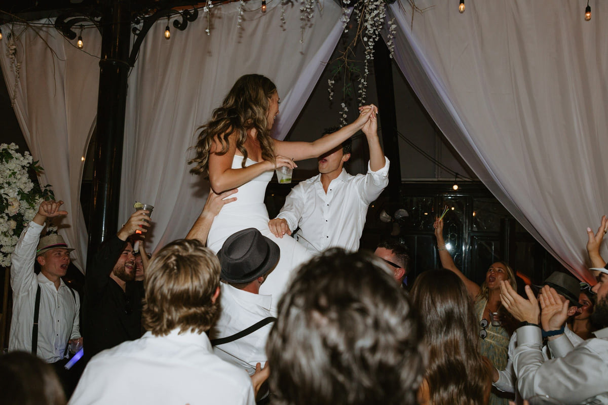 A bride lifted above a packed dance floor with guests' arms in the air