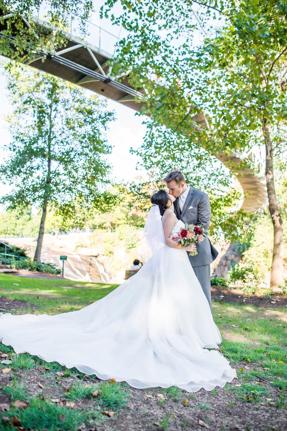 A couple standing beneath a bridge surrounded by green trees in a city park
