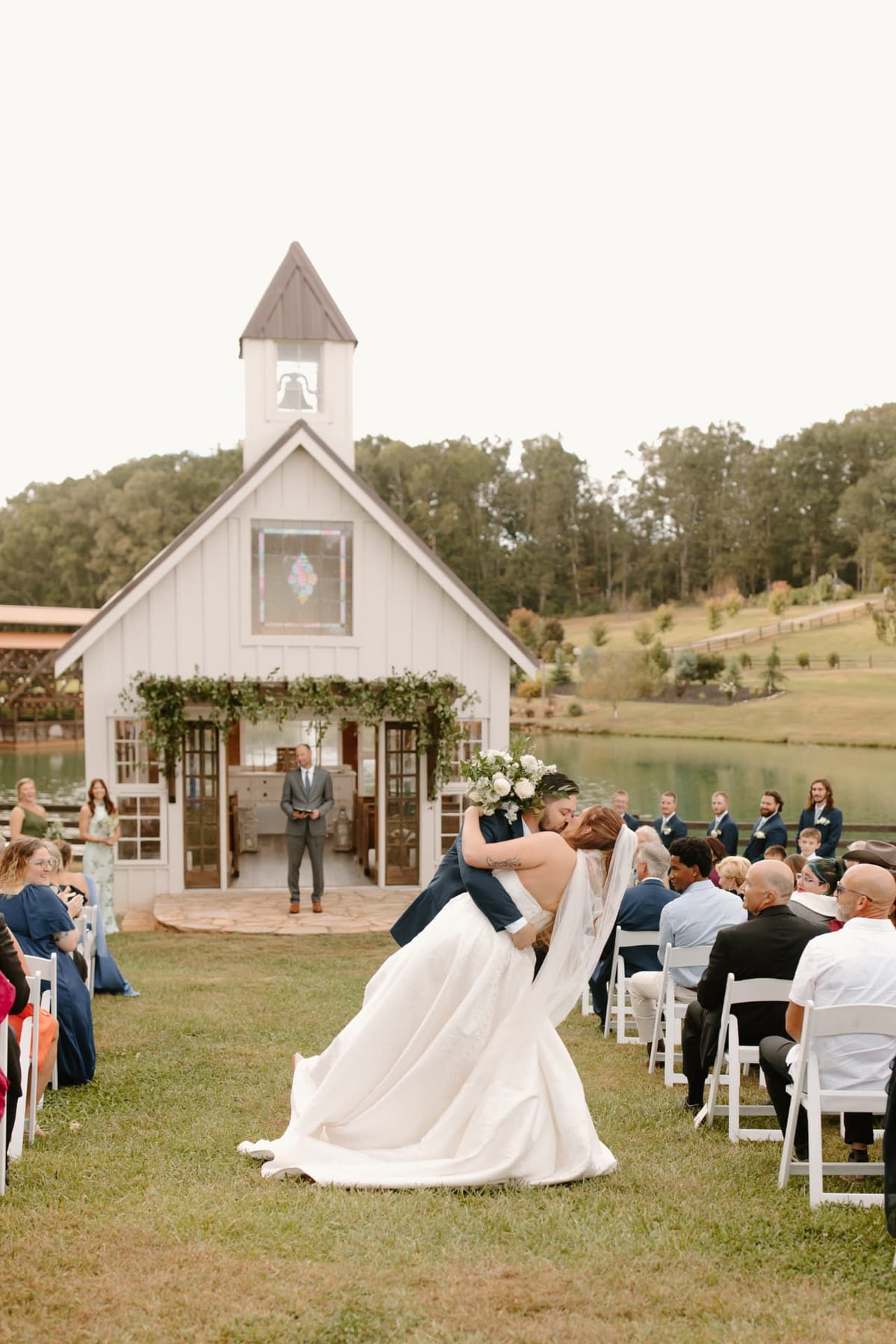 A couple kisses at the end of an outdoor chapel ceremony as guests look on