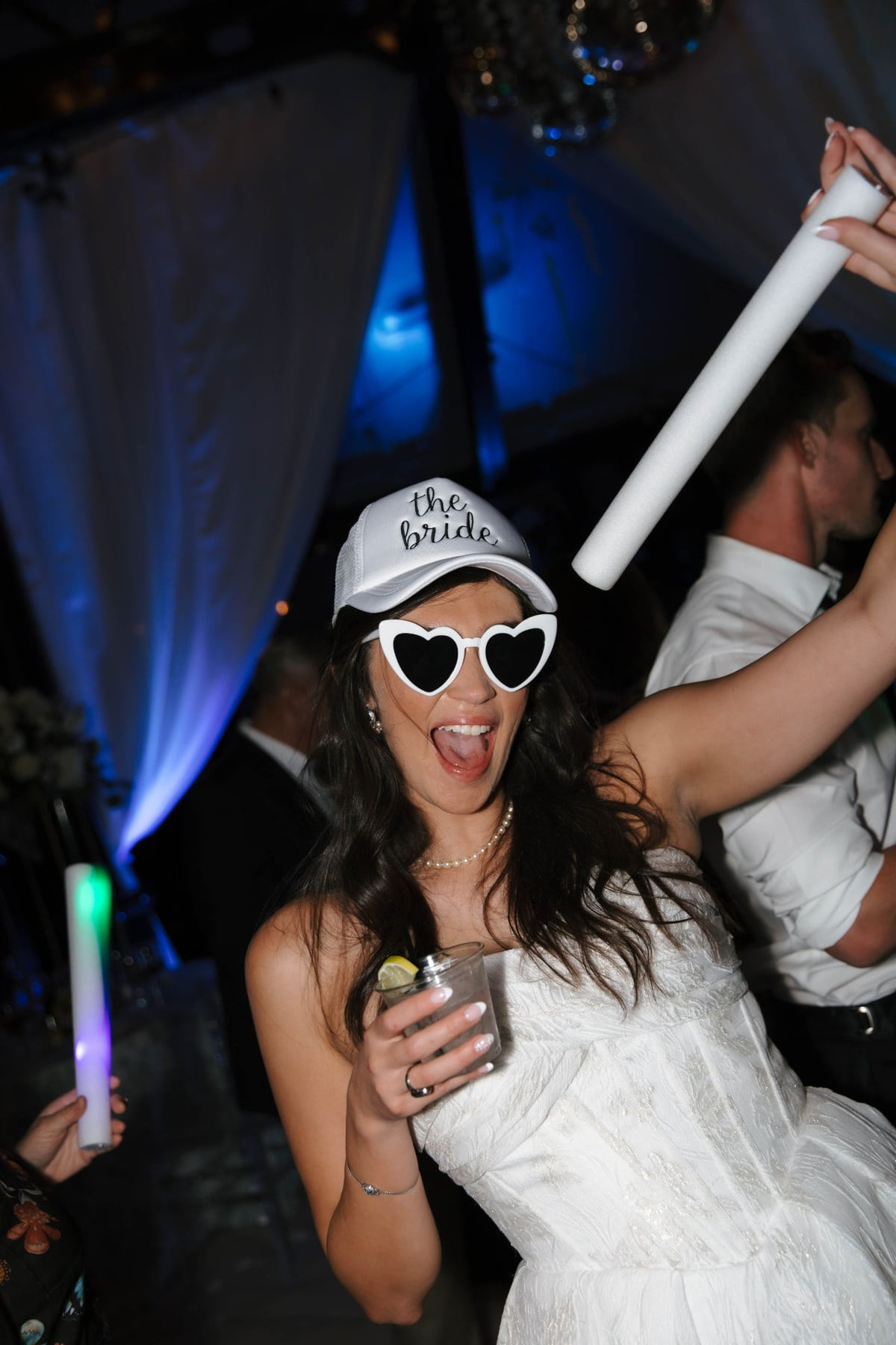 A bride dancing with glow sticks in a reception room lit by blue uplighting