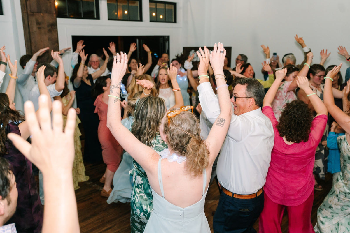 Wedding guests on a packed dance floor with their arms in the air