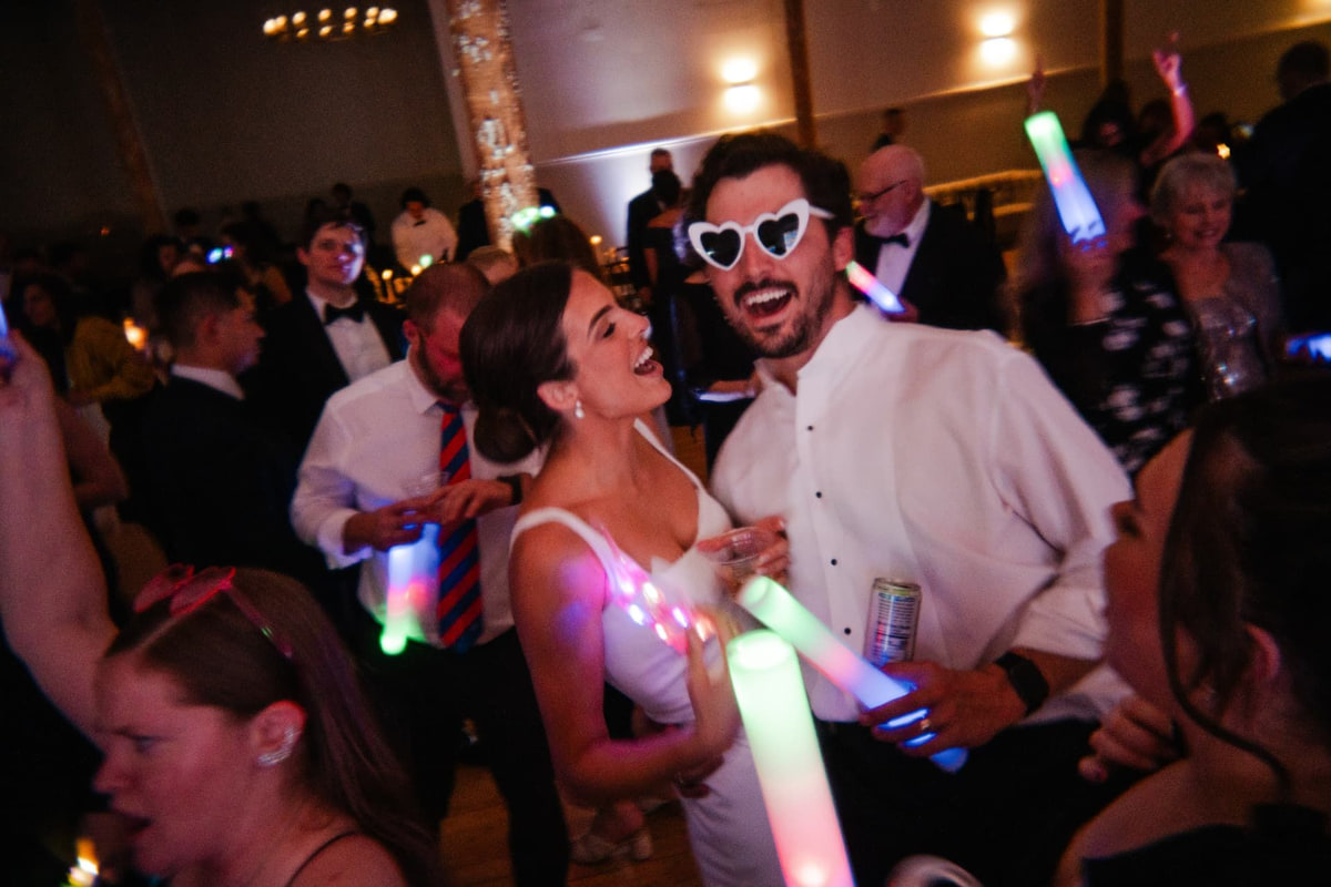 A newly married couple singing along on the dance floor as guests wave glow sticks