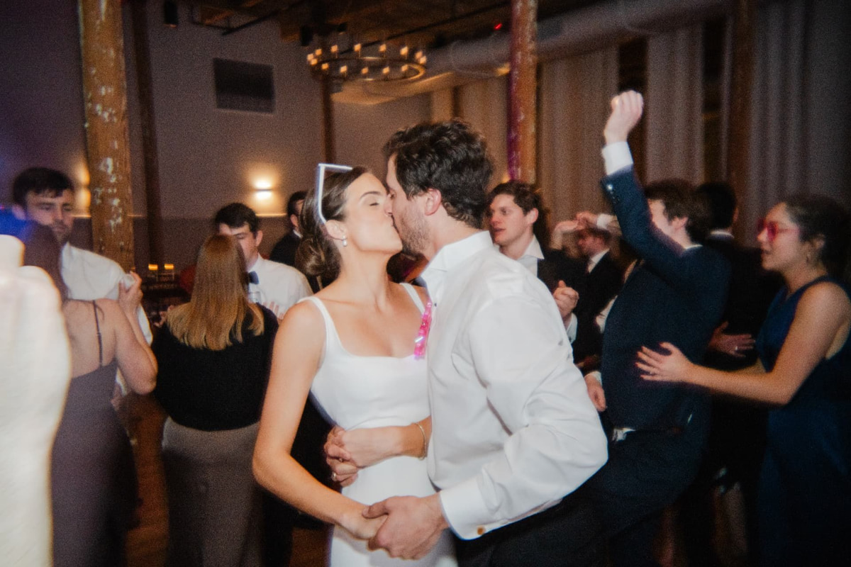 A couple kissing in the middle of a crowded reception dance floor