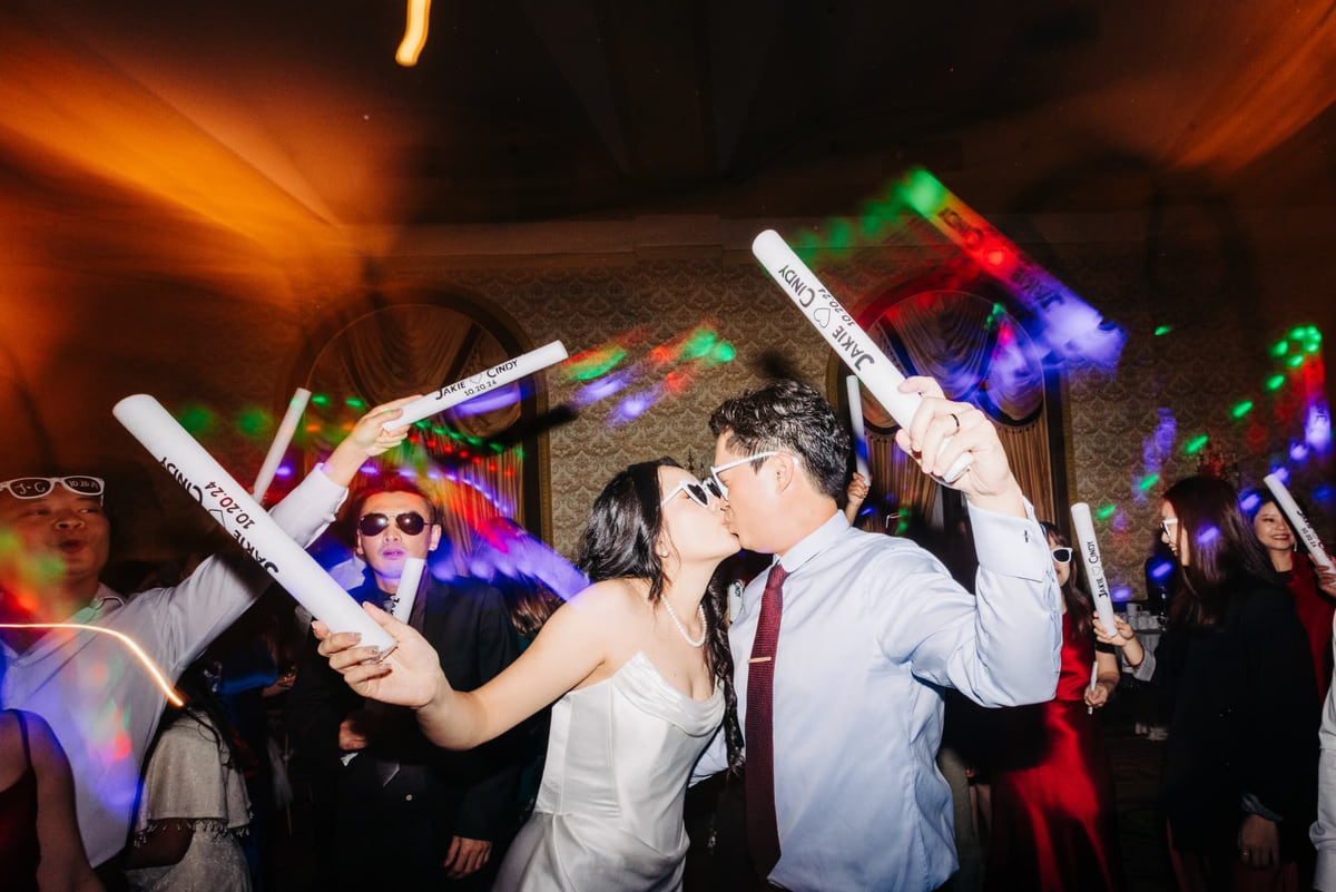 A couple kissing in the middle of a packed dance floor as guests raise glowing foam batons around them